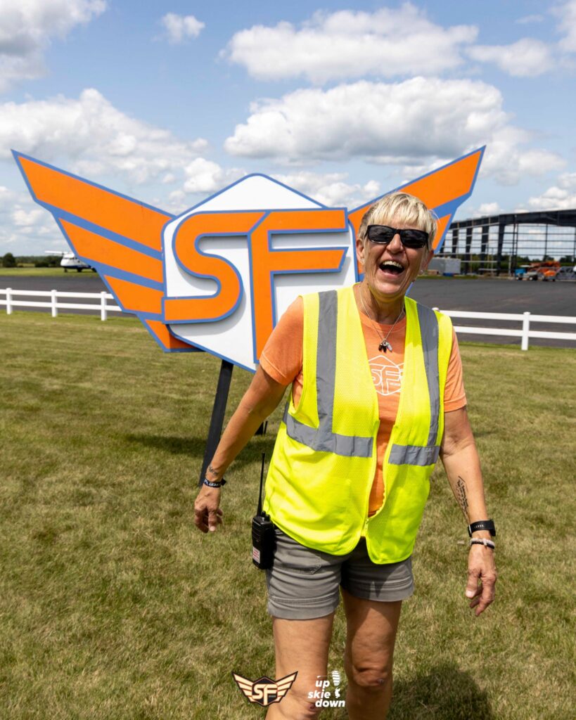 Christa Cross smiling in front of the SDC Summerfest logo at Skydive Chicago